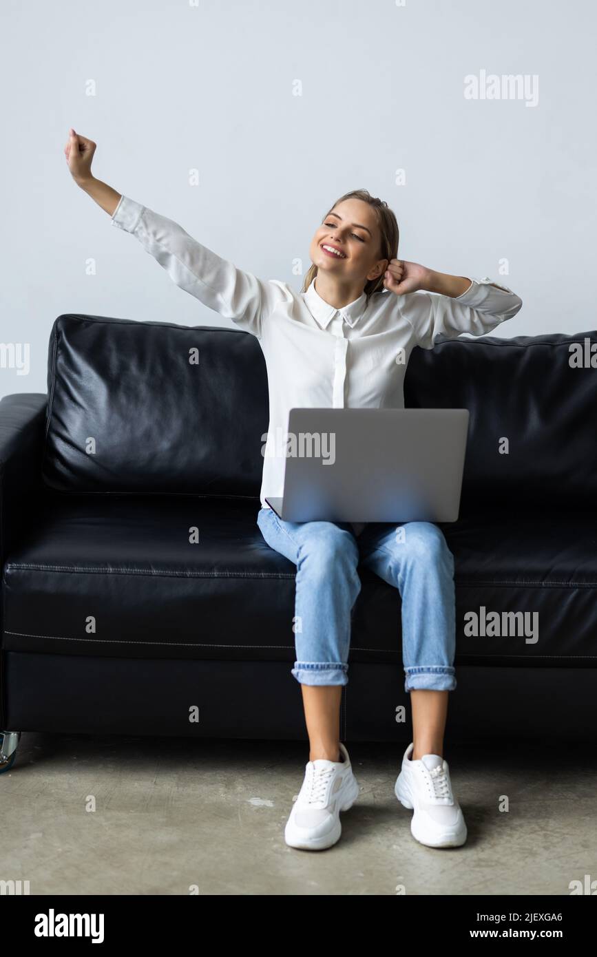 young pretty woman working from home sitting on couch stretching arms happy and smiling Stock Photo