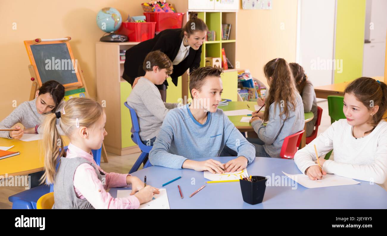 Teacher helping to group of elementary age children drawing Stock Photo ...