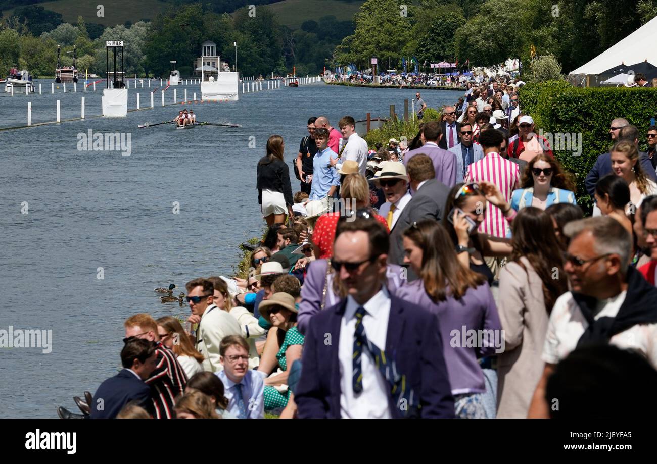 A rowing crew makes their way down to the start as people walk along the river bank on the opening day of the 2022 Henley Royal Regatta alongside the River Thames. Picture date: Tuesday June 28, 2022. Stock Photo