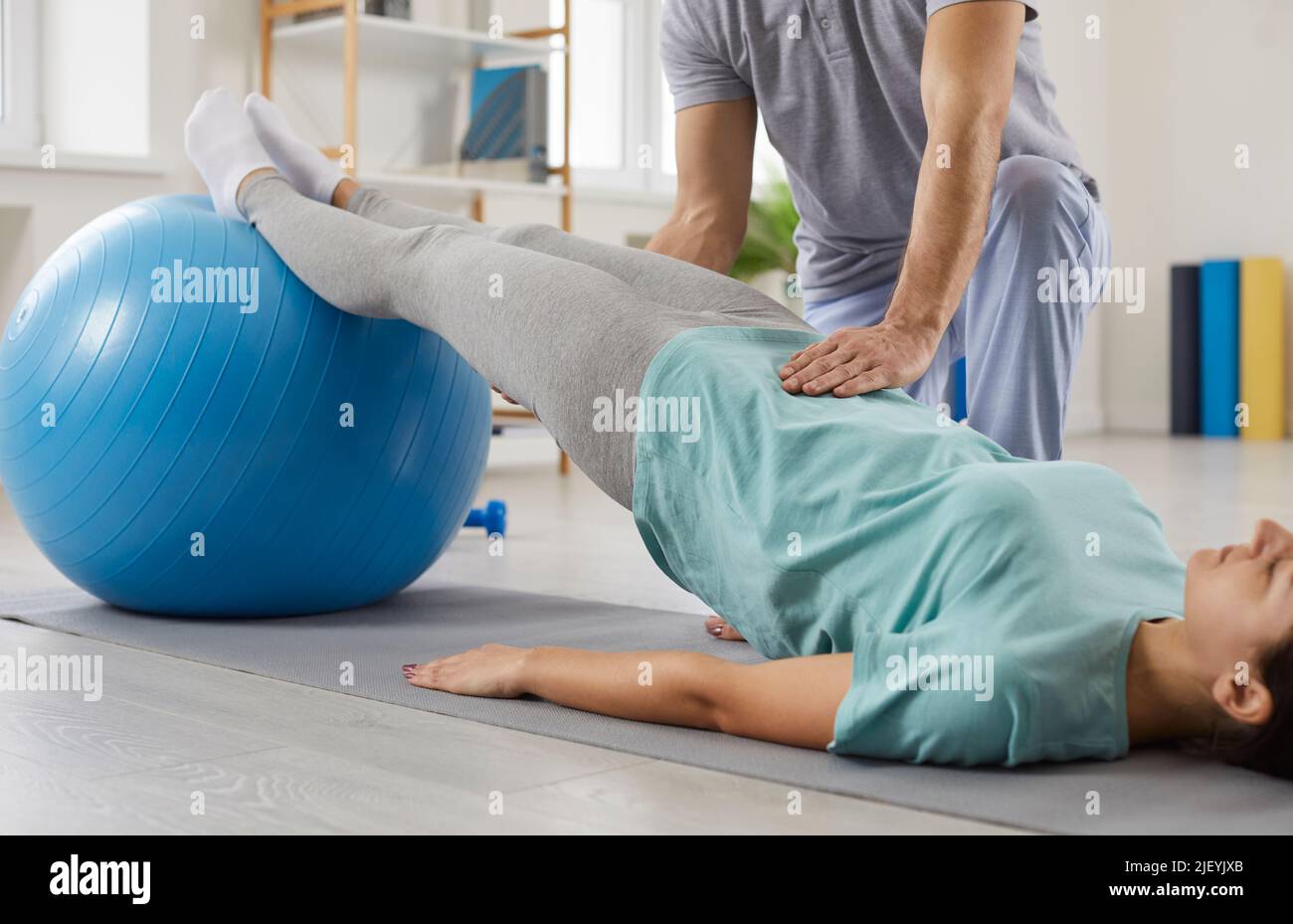 Physiotherapy specialist helping young woman do rehabilitation exercises with fit ball Stock Photo