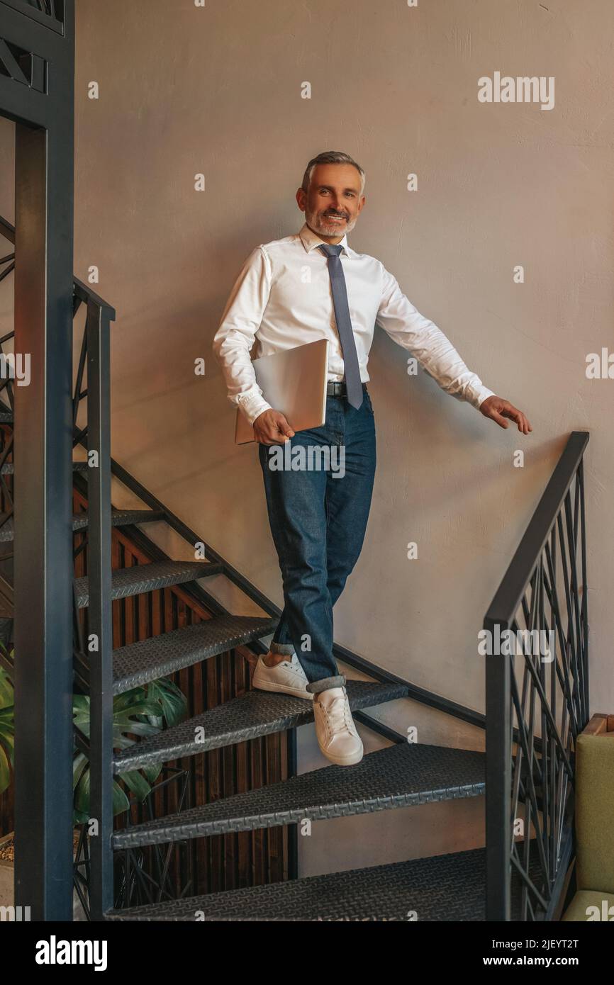Man with laptop walking down stairs looking at camera Stock Photo