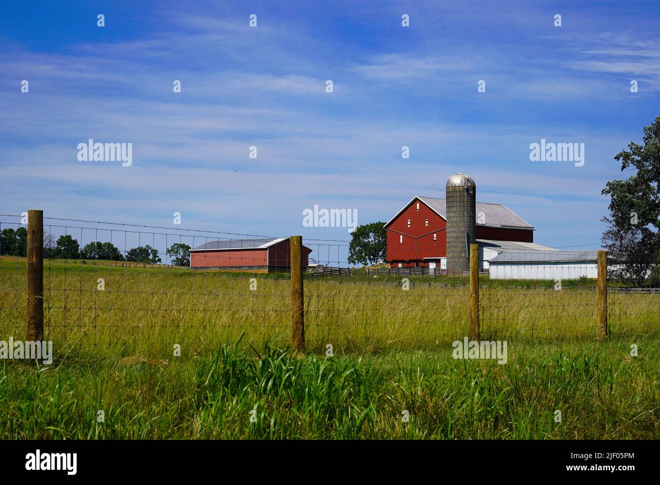Red barn with a silo next to a field Stock Photo