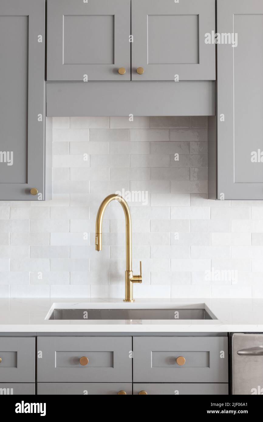 A kitchen sink detail shot with a gold faucet, marble backsplash, grey