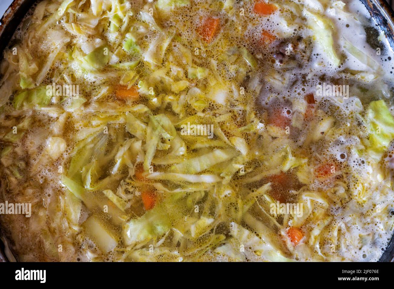 The texture of boiling soup. The food is cooked on the kitchen stove. A delicious soup of cabbage, potatoes, onions, carrots, green peas, chicken live Stock Photo