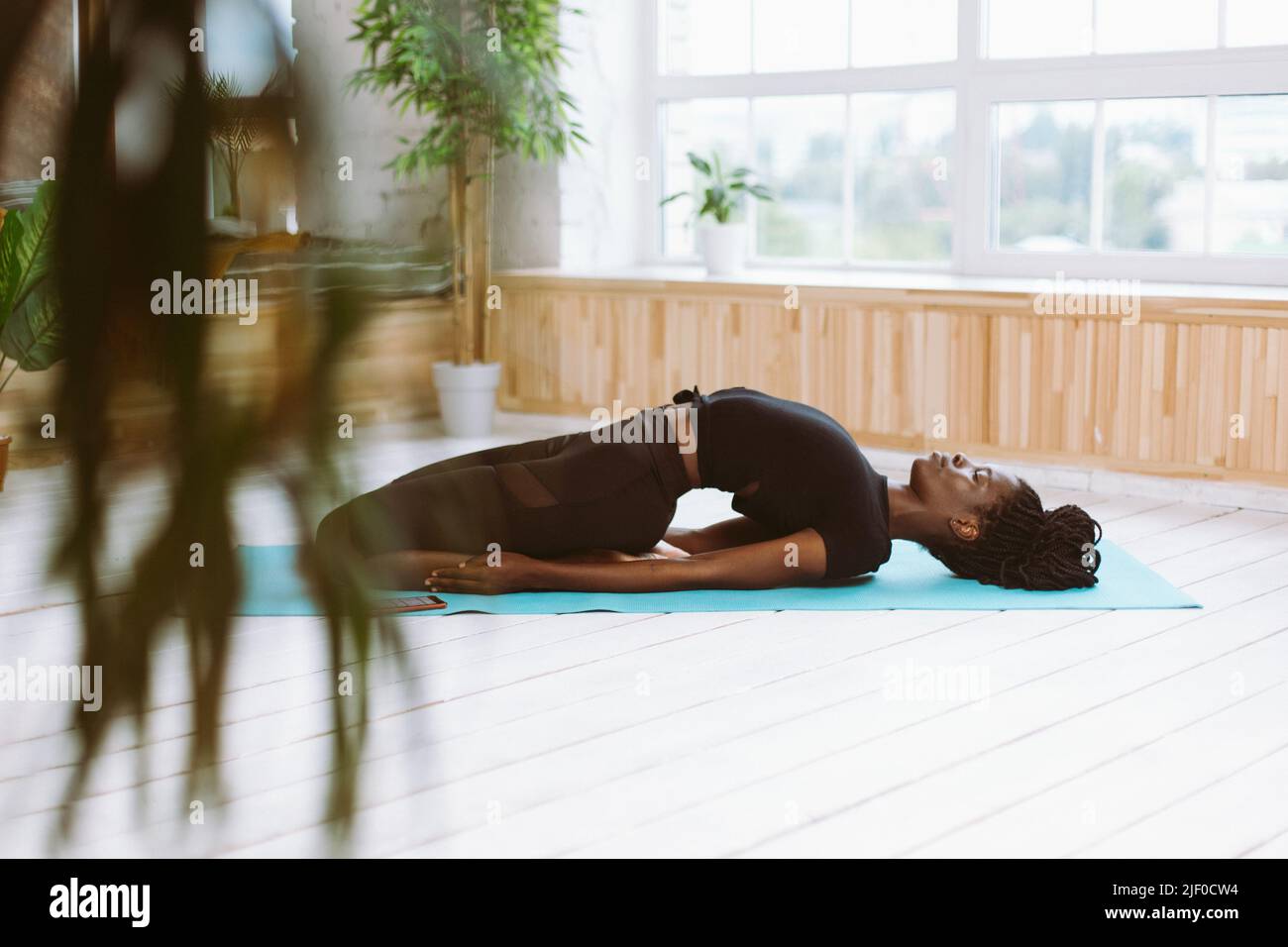 Calm spiritual athlete multiracial woman practicing yoga, stretch on blue mat in gym. Trying to do reclining Hero pose Stock Photo