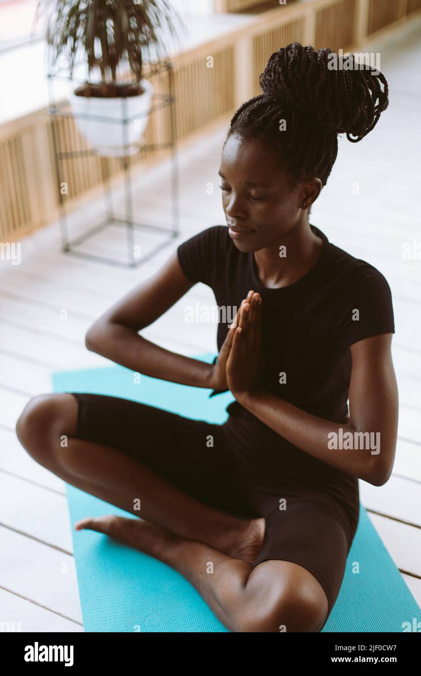 Vertical meditating, spiritual multiracial woman with hands in namaste Asana pose, sit in yoga lotus greeting posture Stock Photo
