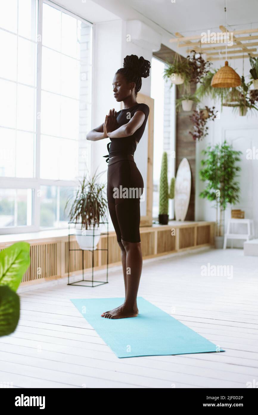 Vertical joyful meditating young African American woman in black sportswear practicing yoga, keep hands in namaste mudra Stock Photo