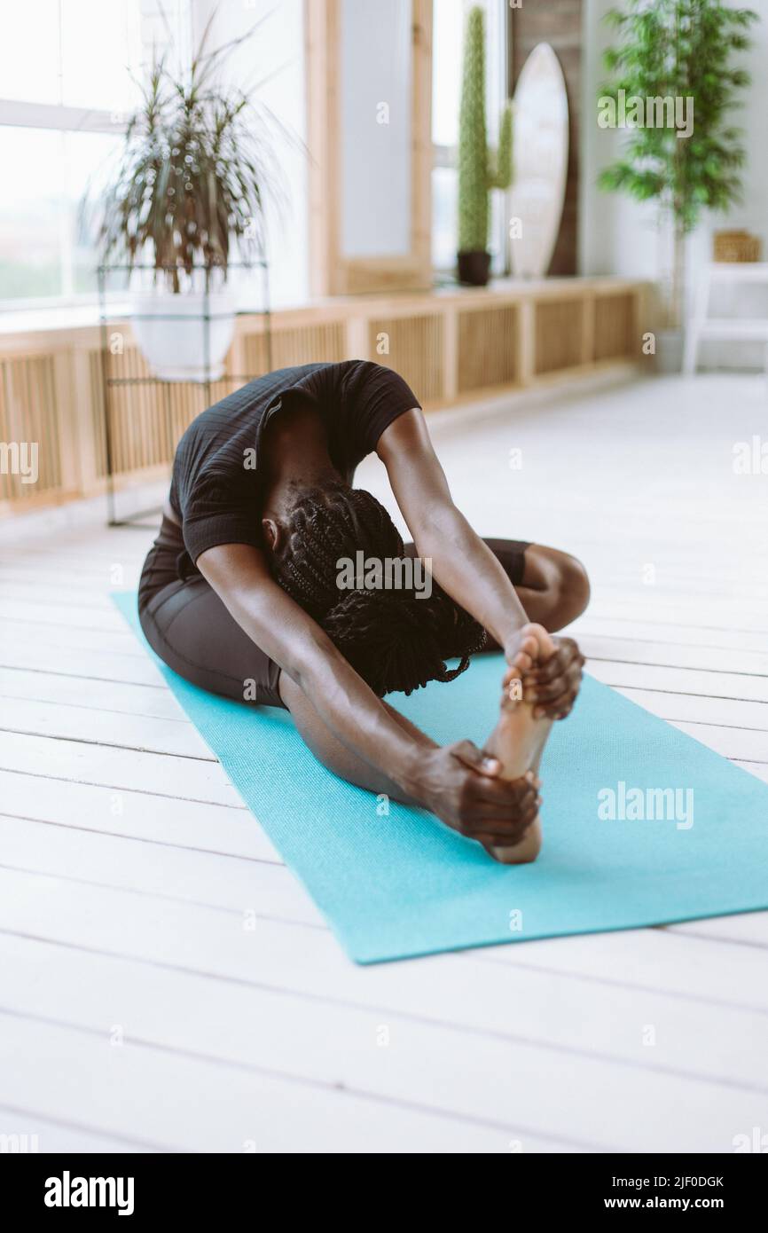 Sportive athlete healthy and mindful multiracial woman with dreads in black sportswear practicing yoga seated side bend  Stock Photo