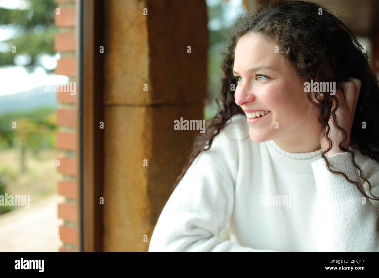 Happy female looks through a window sitting in a house interior Stock Photo