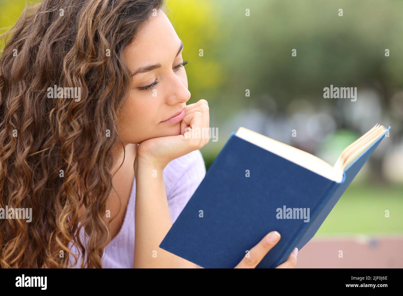 Relaxed woman reading a book sitting in a park alone Stock Photo