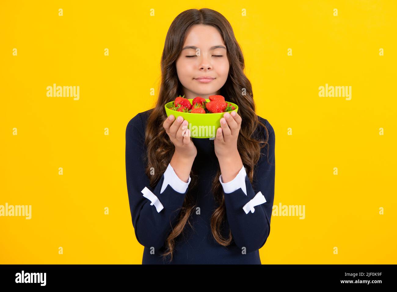 Child eating a strawberries. Happy smiling teen child hold strawberry bowl on yellow background. Healthy natural organic vitamin food for kids Stock Photo