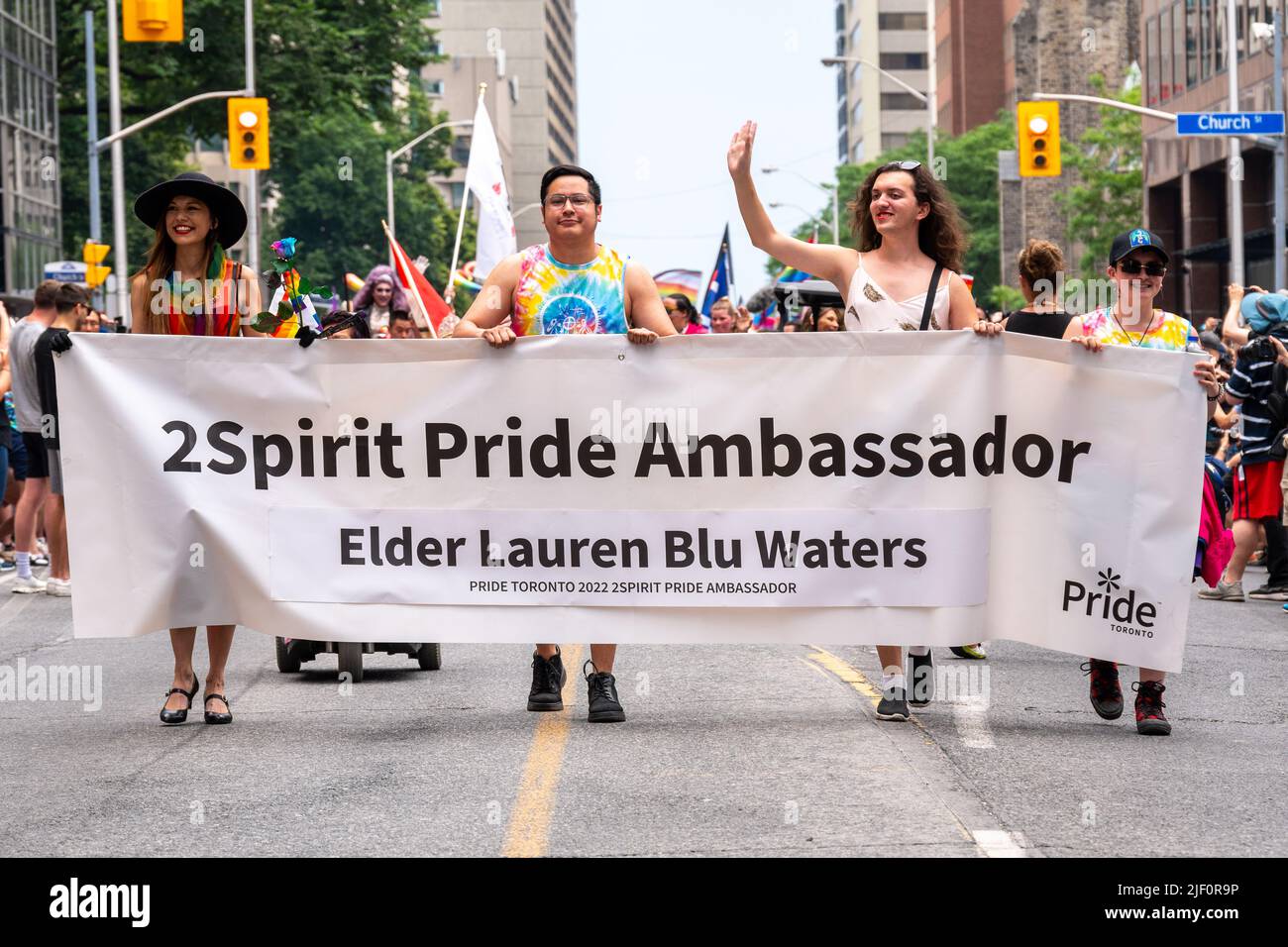A group of people holding a banner announcing the 2Spirit Pride Ambassador Elder Lauren Blue Waters. They are marching in Bloor Street during Pride Pa Stock Photo