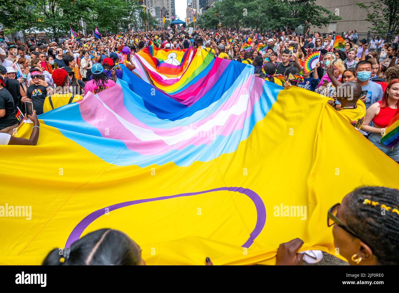 A giant textile flag including diverse symbols of the LGBTQ+ community is surrounded by a crowd of people in Bloor Street during Pride Parade. Stock Photo