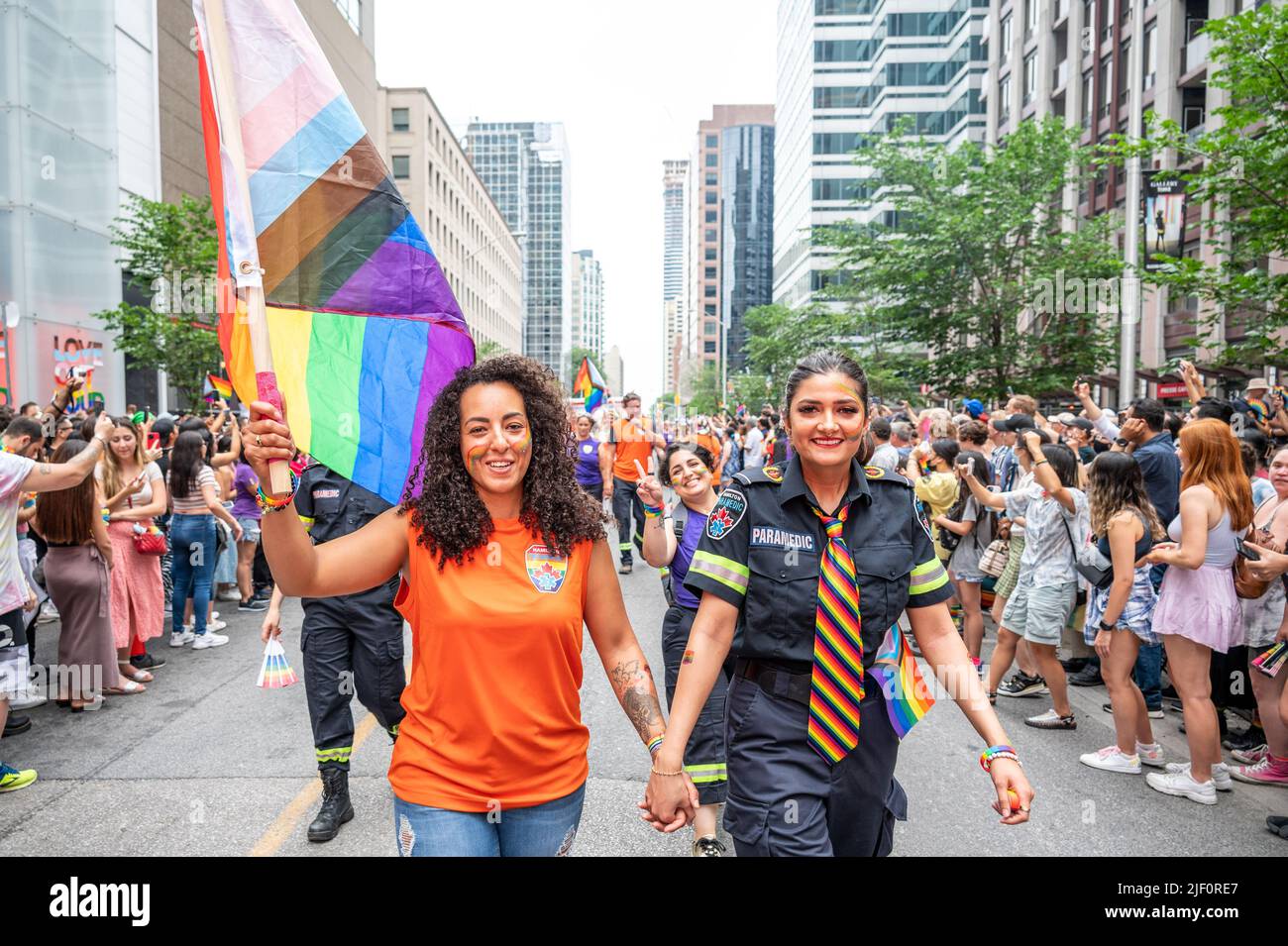 Two female people holding hands and holding the Progressive Pride Flag walk in Bloor Street during Pride Parade. Stock Photo
