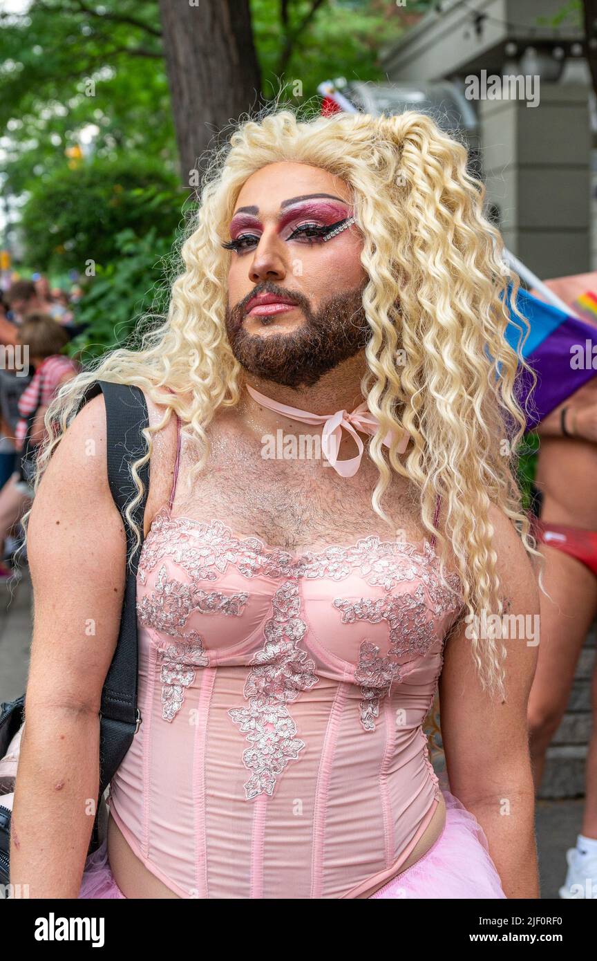 A person in a pink dress, blonde wig, and a beard partakes in the Pride Parade Stock Photo