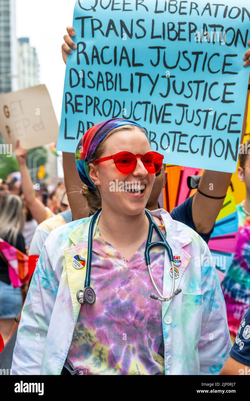 A happy female medicine doctor wears rainbow clothes and marches as part of the LGBTQ Doctors and Allies bloc during Pride Parade Stock Photo