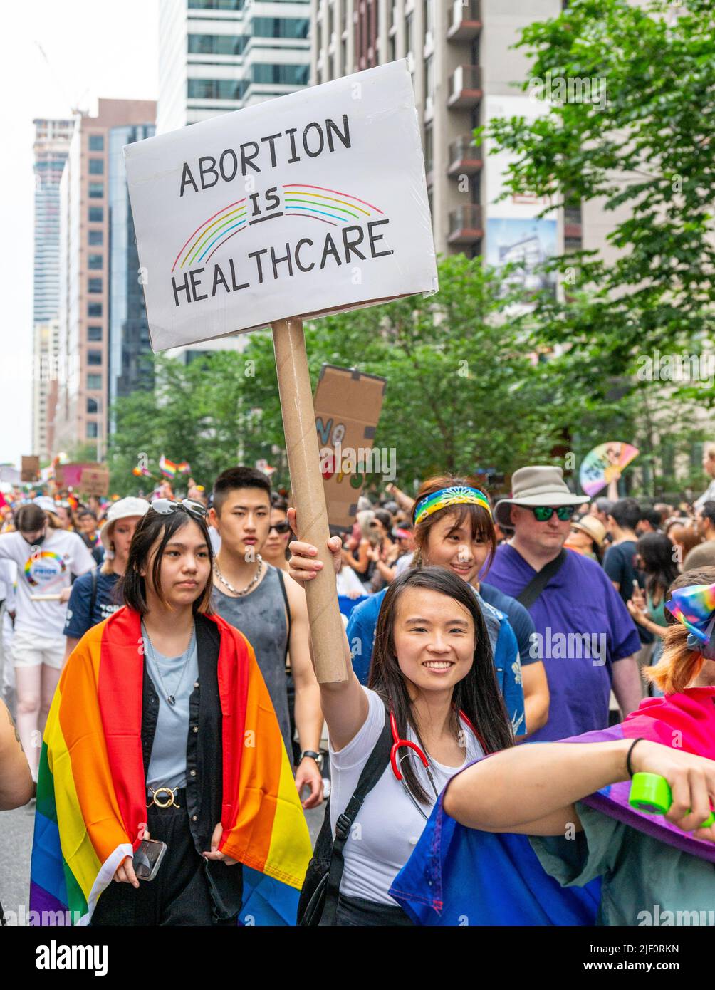A woman of Asian descent holds a sign reading 'Abortion Is Healthcare' as she marches during Pride Parade. Stock Photo