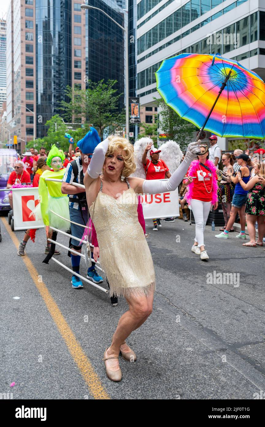 A senior person wearing a dress and a rainbow umbrella marches in Bloor Street during Pride Parade Stock Photo