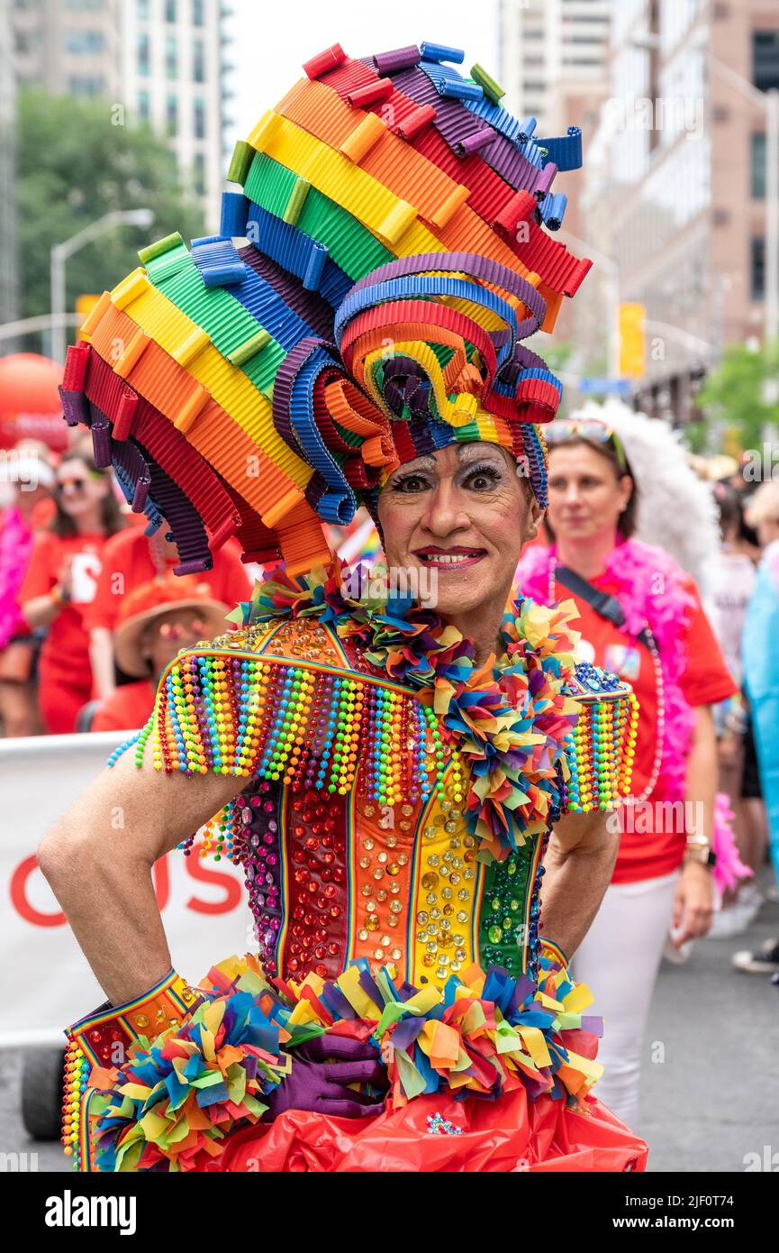 A person wearing multi colored clothes smiles to the camera while marching in the Pride Parade. Stock Photo