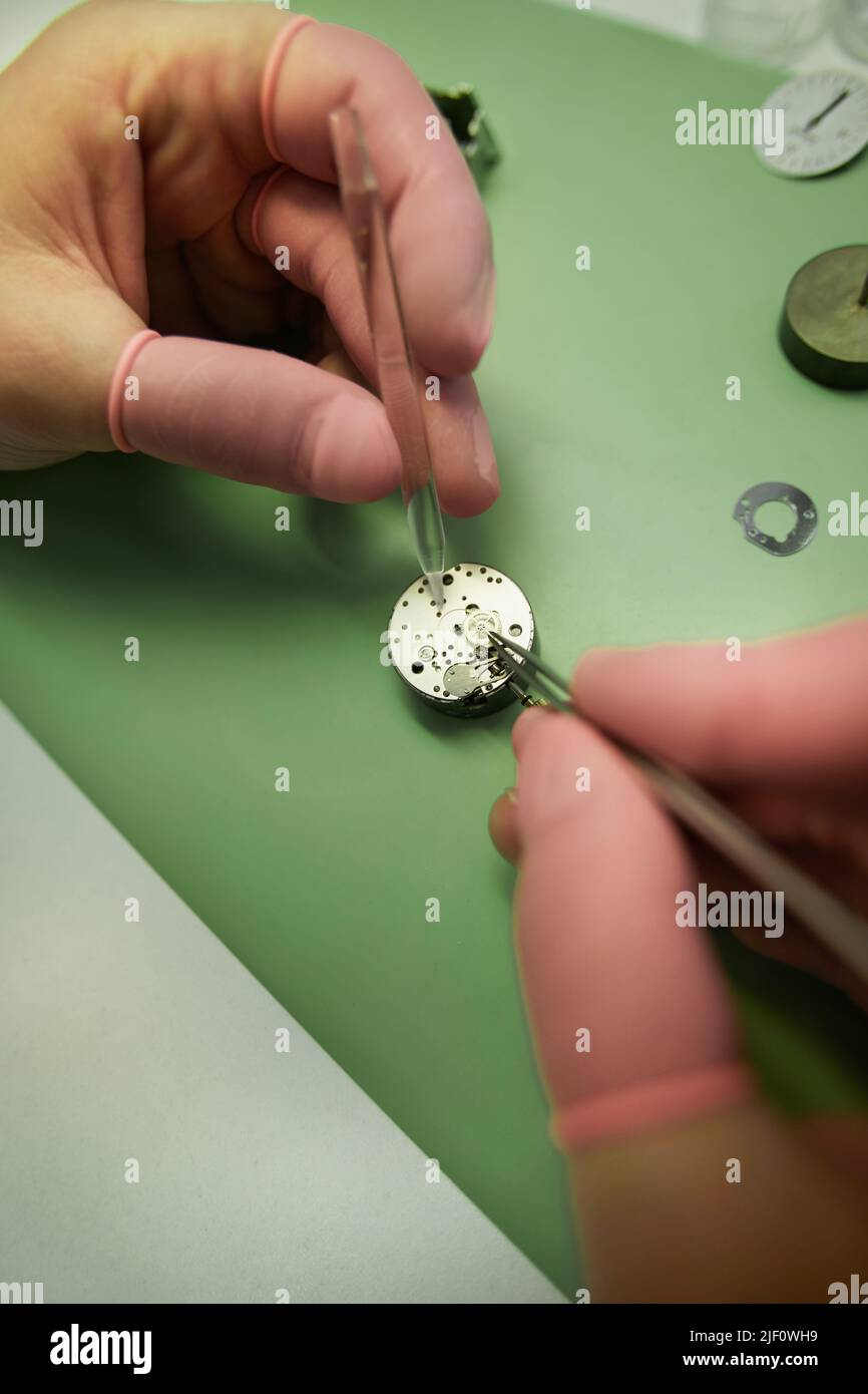 Close-up of unrecognizable engineer in pink finger gloves using dropper and tweezers while adding lubricant into watch movements Stock Photo