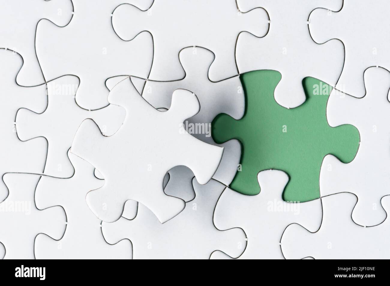 White jigsaw puzzle with missing piece on green background. Copy space. Stock Photo