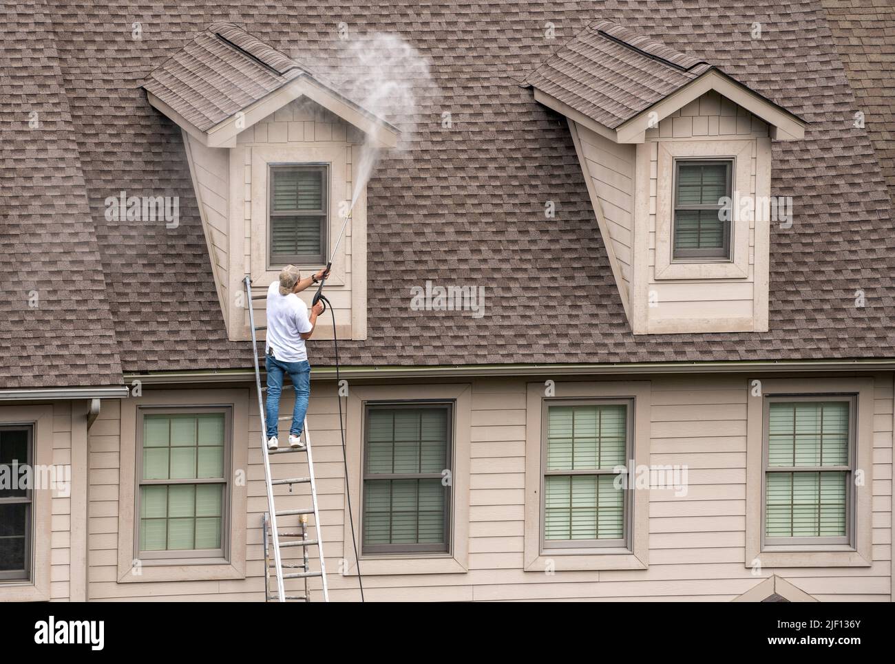 Painter on ladder using pressure wash spray to clean woodwork before