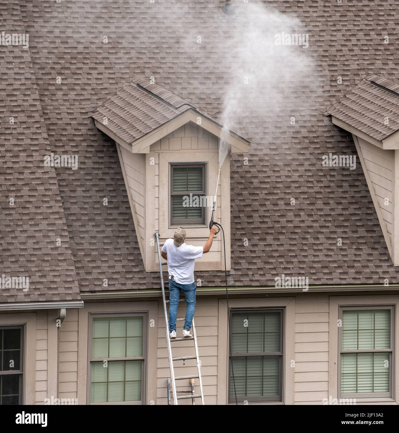 Painter on ladder using pressure wash spray to clean woodwork before