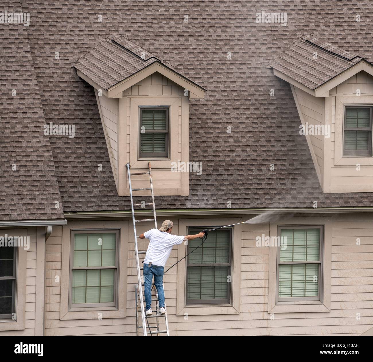 Painter on ladder using pressure wash spray to clean woodwork before