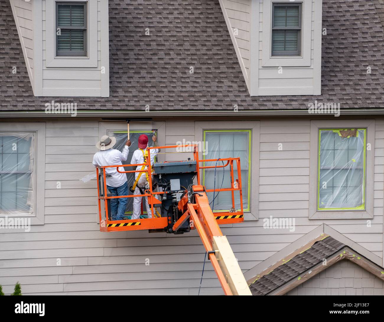 Two home painters in articulating boom lift spray painting townhouse