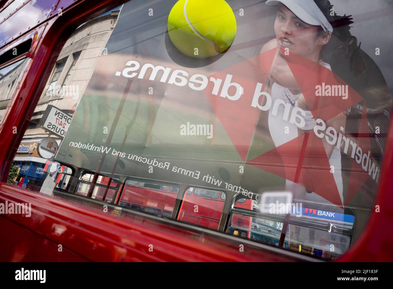 Reflected in the window of a bus, British tennis player, Emma Raducanu appears on a giant billboard in Wimbledon town centre, on the second day of competition during the Wimbledon Lawn Tennis Association championships, on 28th June 2022, in London, England. Stock Photo