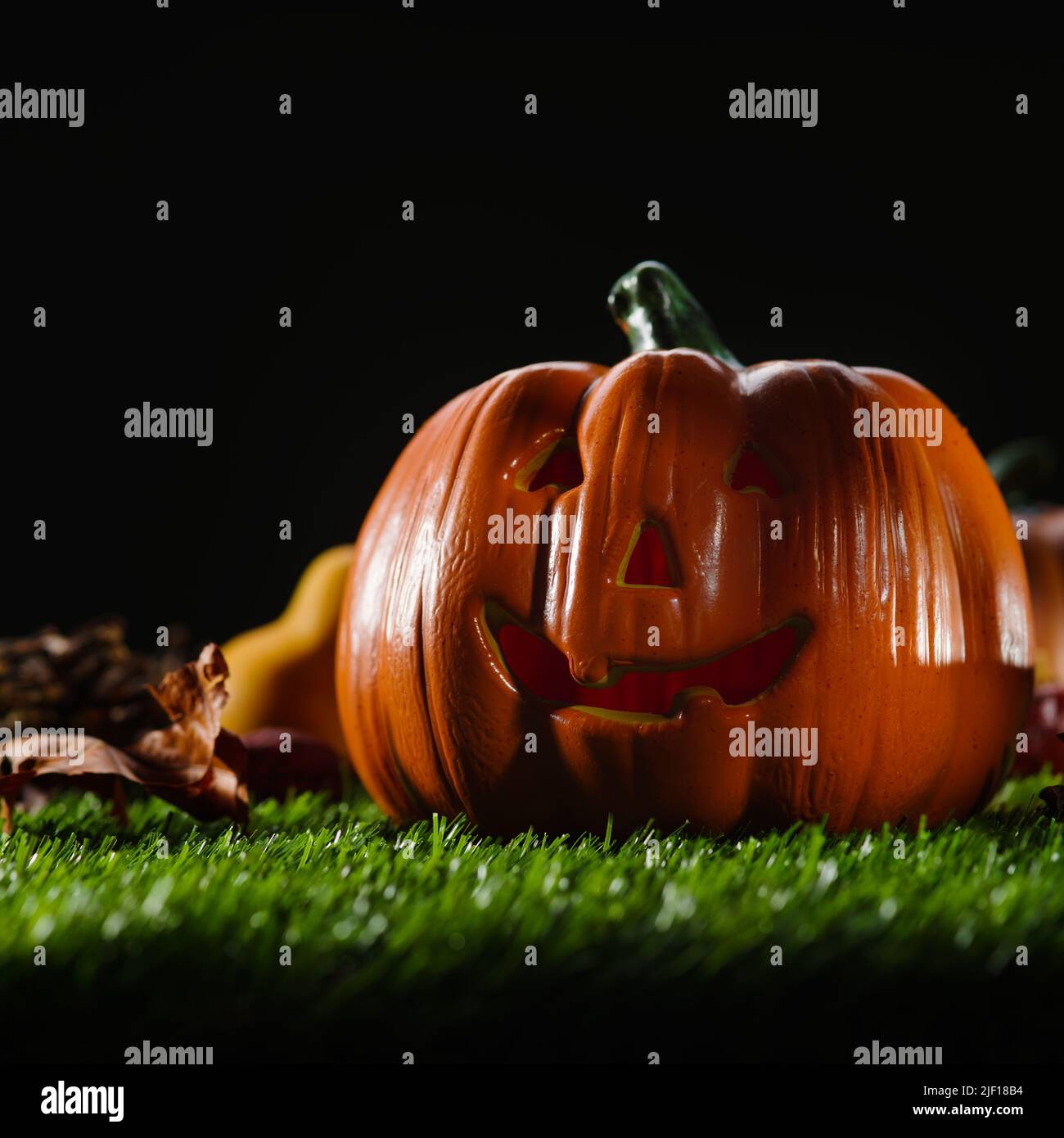 On a green lawn, an orange smiling Halloween pumpkin, cones and autumn leaves against a black gloomy night sky. Celebration of the autumn holiday - Ha Stock Photo