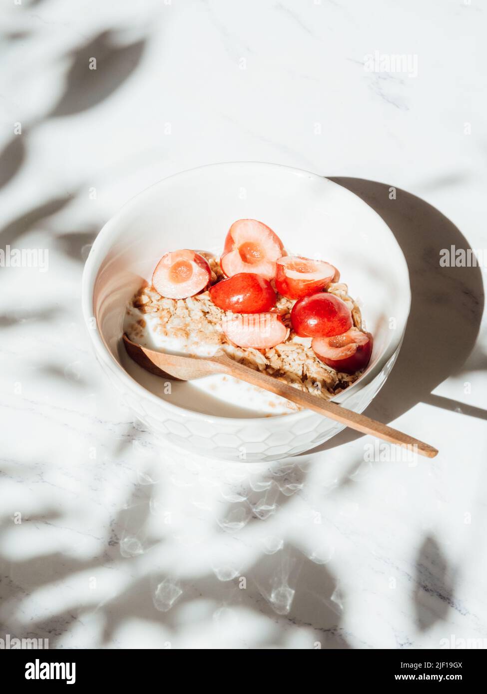 Healthy breakfast with greek yogurt, granola and cherry on bright background in sunlight and the shadows of the leaves of the tree, Health care Stock Photo