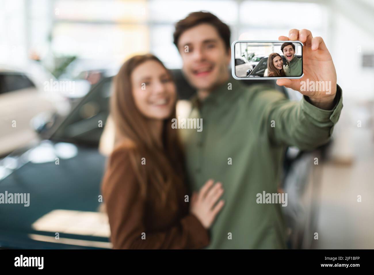 Joyful young Caucasian couple taking selfie after buying new auto at dealership, selective focus Stock Photo