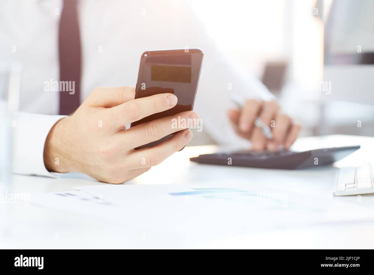 Close-up of unrecognizable white collar worker sitting at desk with paper and reading notification in phone Stock Photo