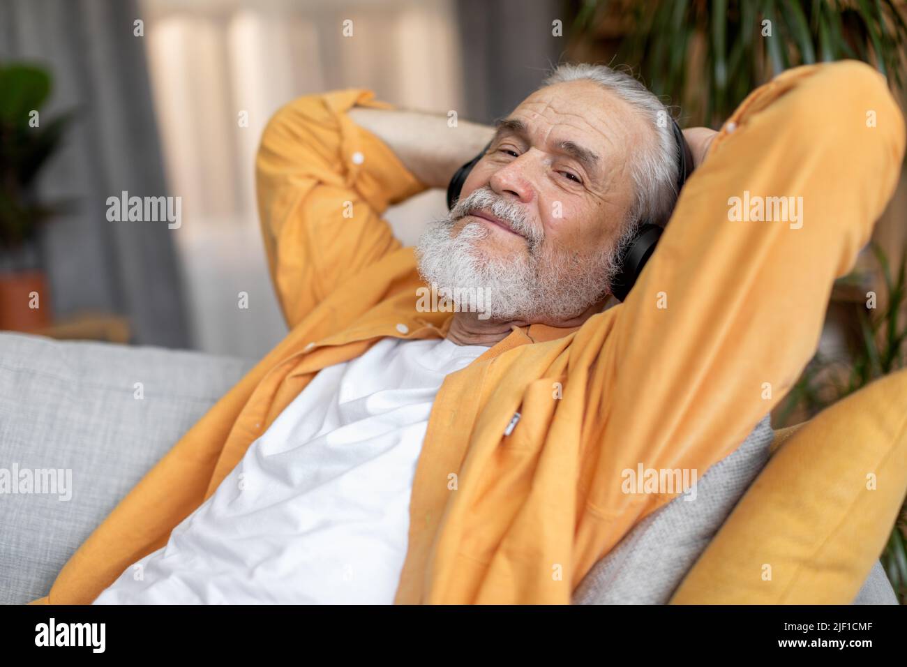 Good-looking elderly man enjoying newest wireless headset at home Stock Photo