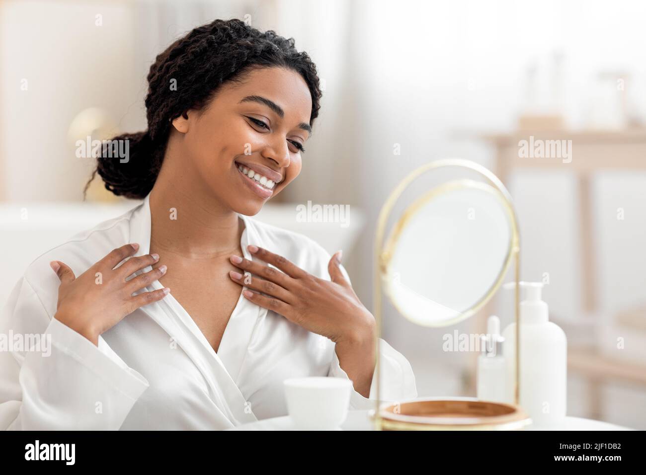 Beautiful black woman looking in mirror and touching decollete zone Stock Photo