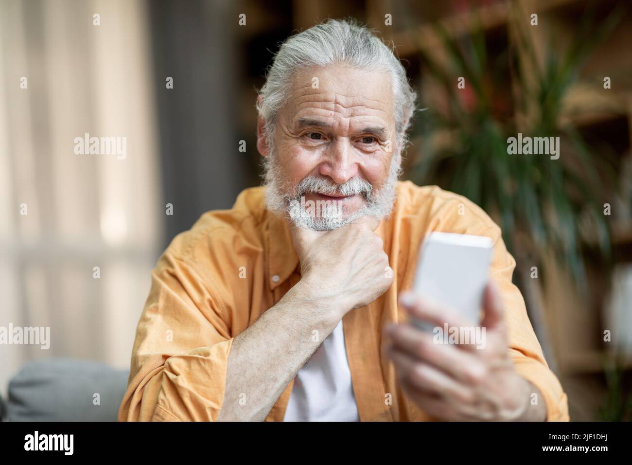 Cheerful senior man using smartphone at home Stock Photo