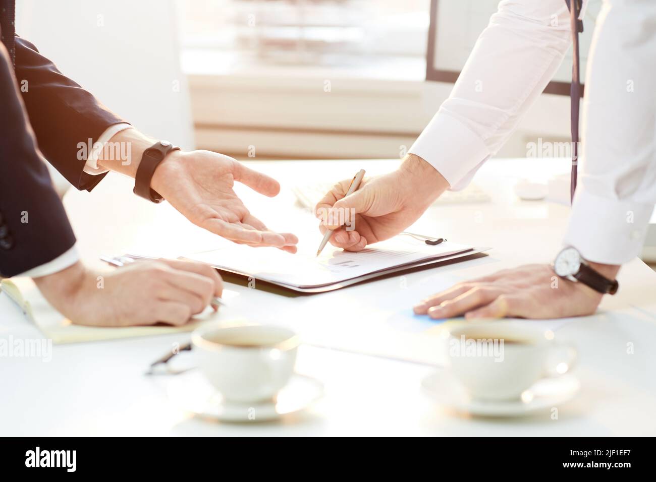 Close-up of unrecognizable business colleagues standing at table and discussing analytical points while viewing papers together Stock Photo