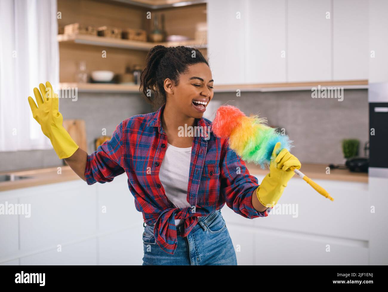 Cheerful young african american female in rubber gloves singing at imaginary microphone and sing song Stock Photo