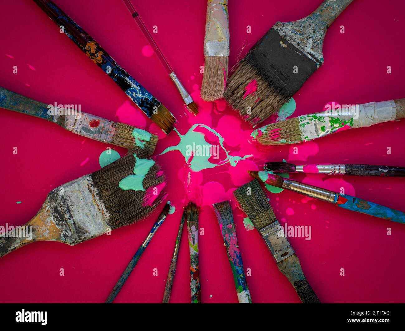 Horizontal composition where some old and used brushes of various sizes appear on a magenta or fuchsia background and with pink and light green paint Stock Photo