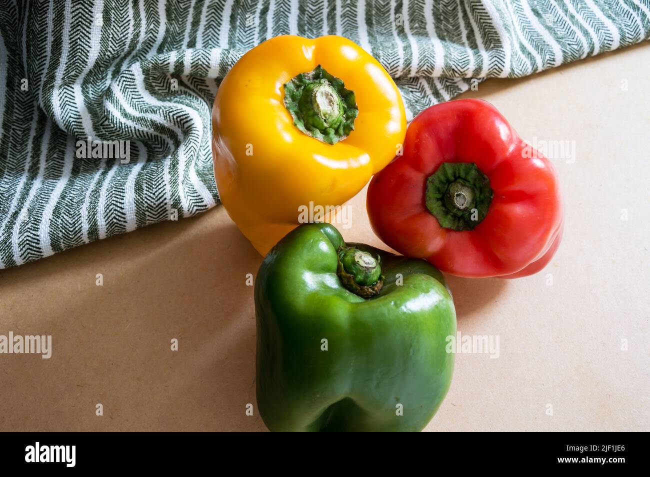 Close-up angled green, red and yellow bell peppers photographed from above next to a striped fabric Stock Photo