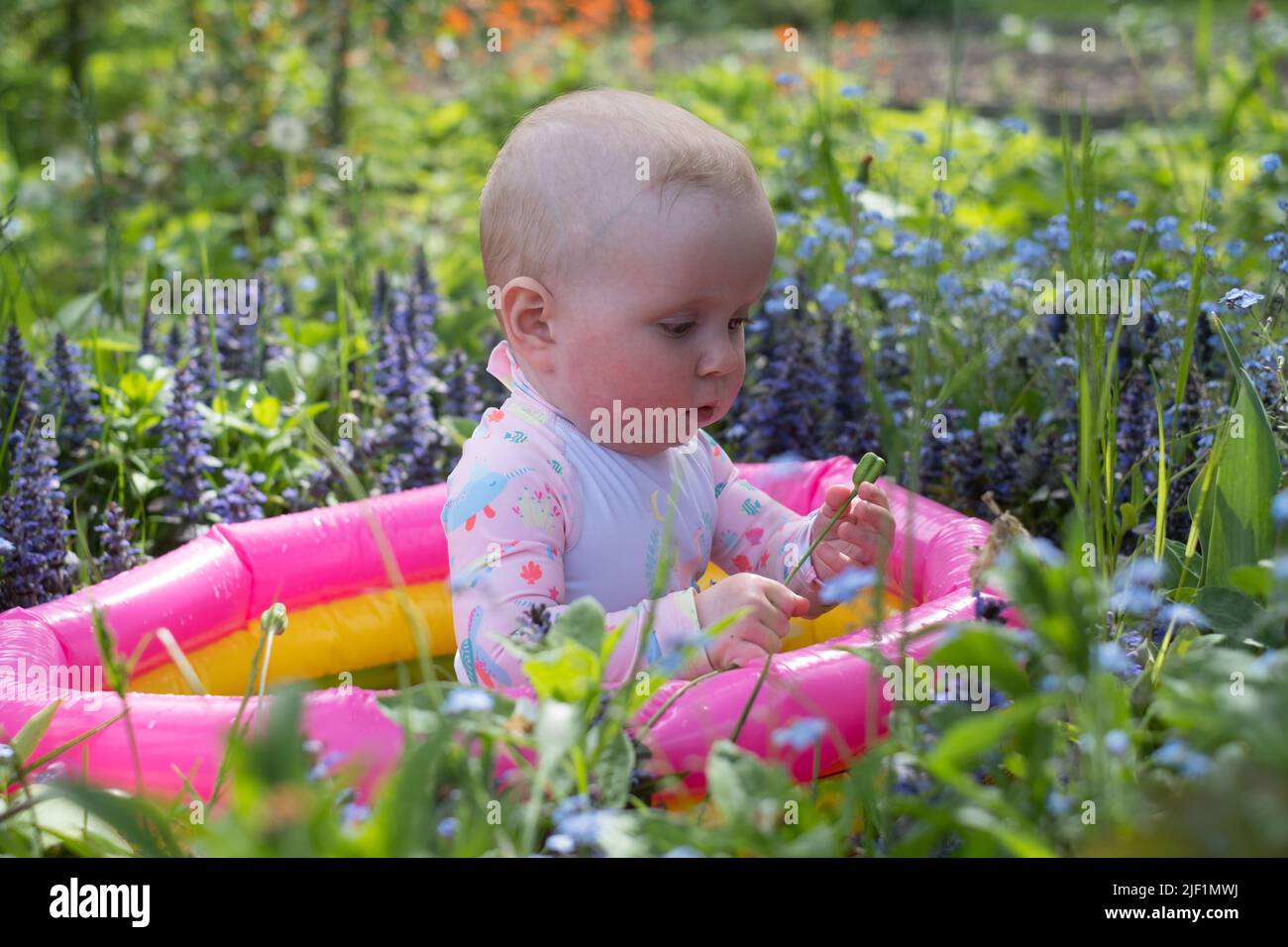 baby is sitting in a bubble bath in the garden on hot summer day. outdoor water treatments. Stock Photo