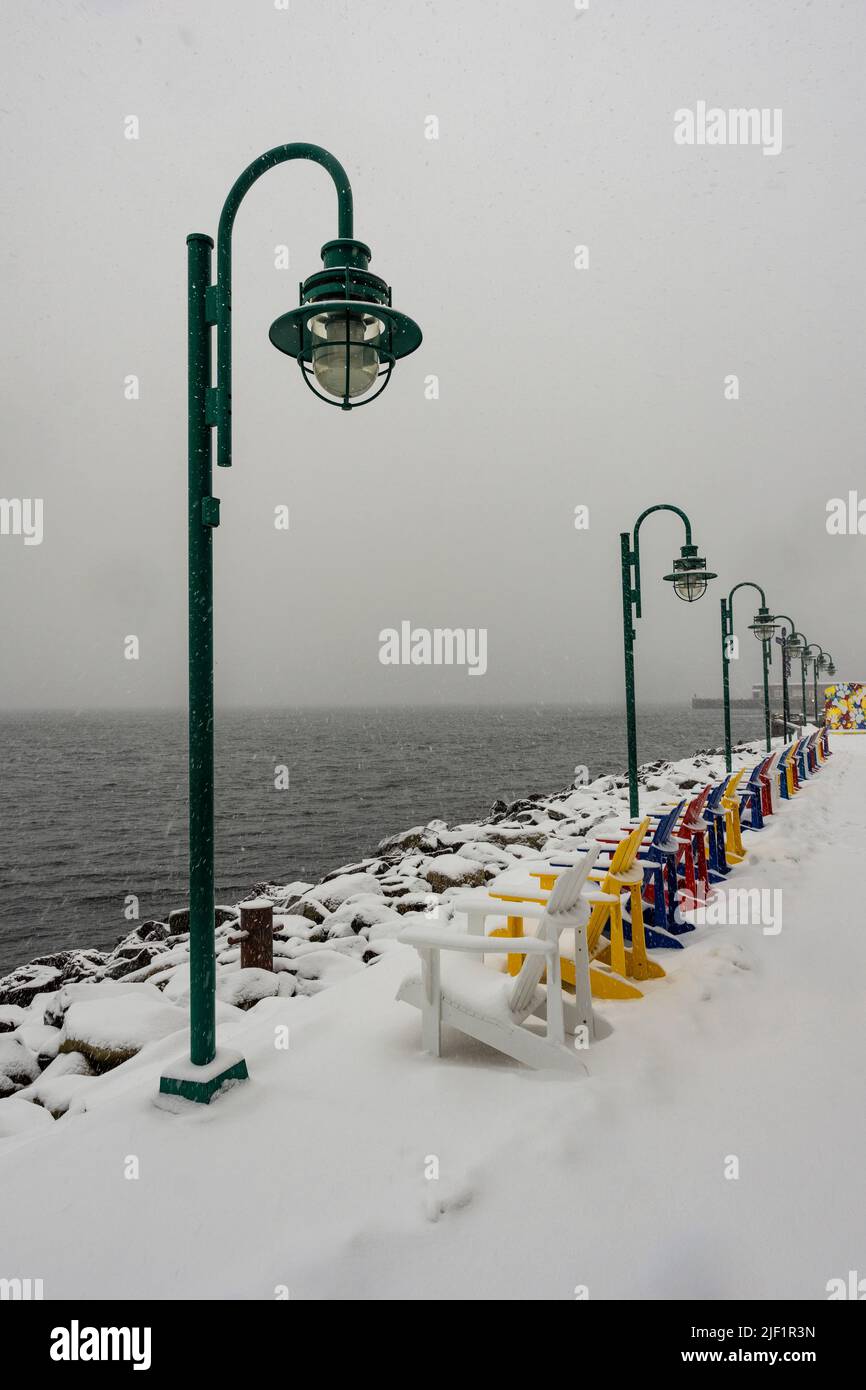 Colourful row of adirondack chairs in snow on the waterfront boardwalk in Halifax, Nova Scotia, Canada. Stock Photo