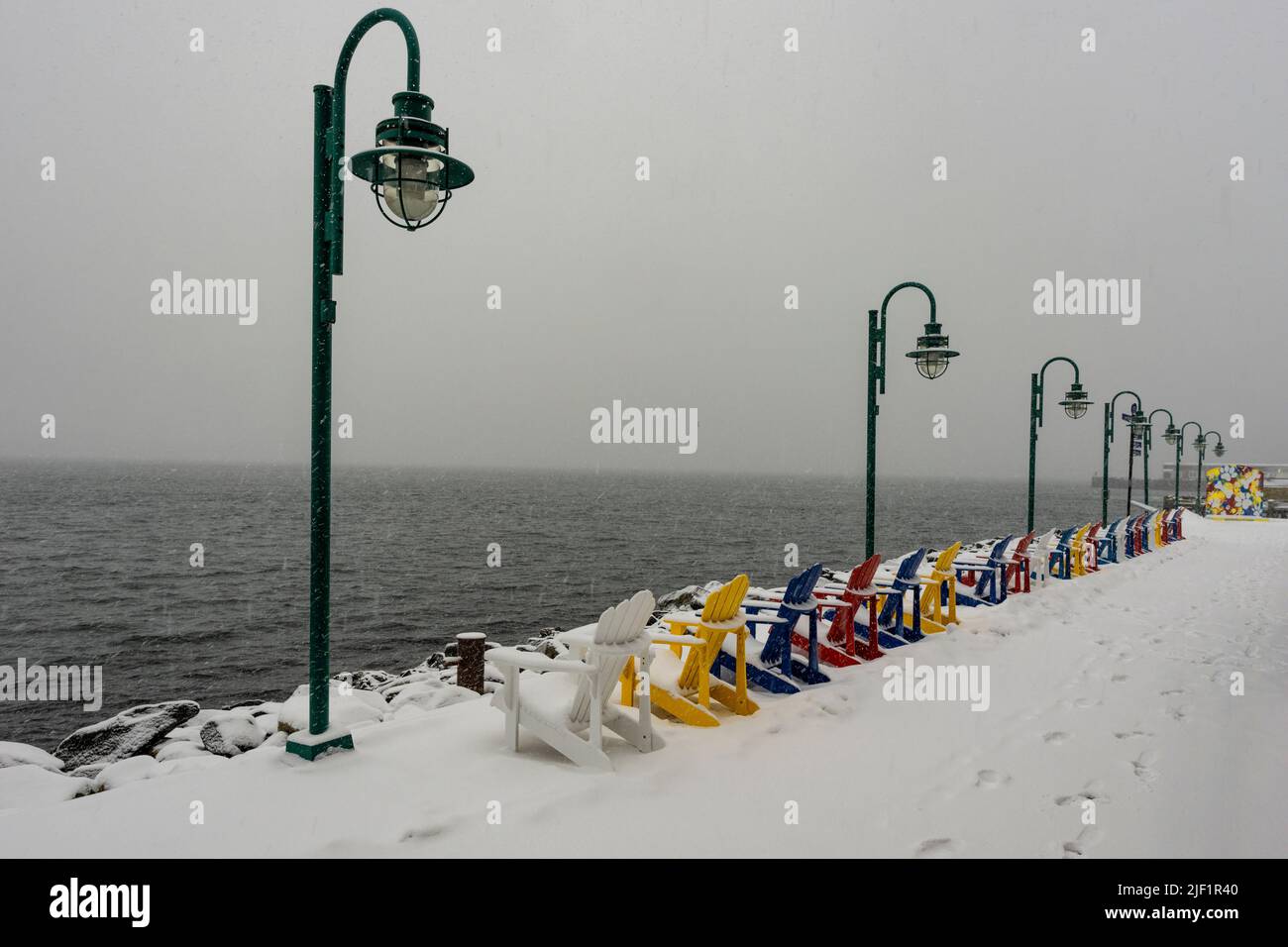Colourful row of adirondack chairs in snow on the waterfront boardwalk in Halifax, Nova Scotia, Canada. Stock Photo