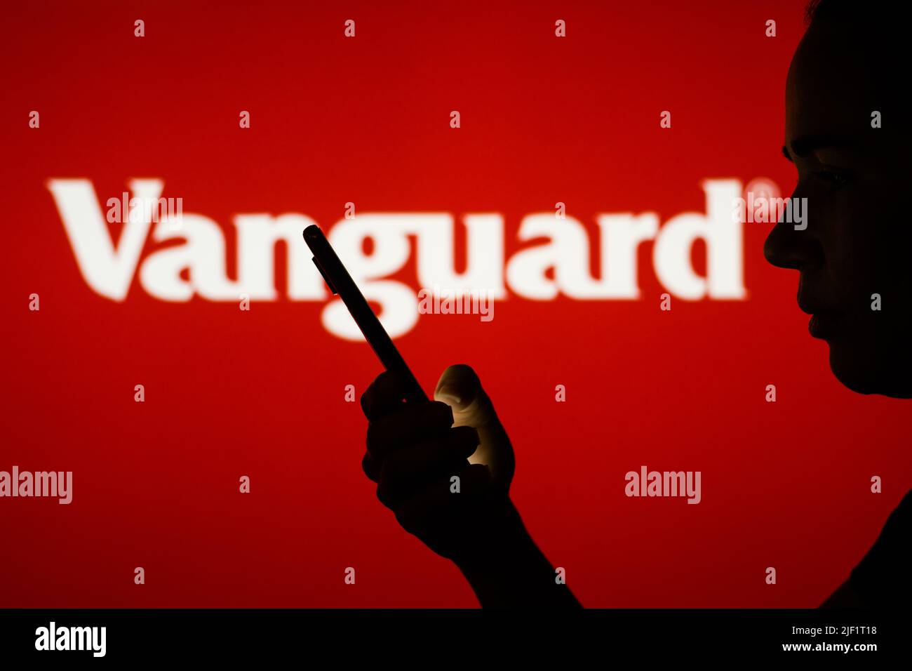In this photo illustration, the Vanguard Group logo is seen in the background of a silhouetted woman holding a mobile phone. Stock Photo
