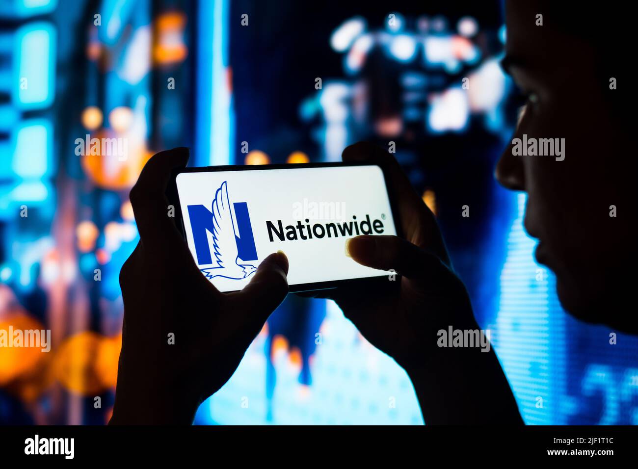 In this photo illustration, a silhouetted woman holds a smartphone with the Nationwide Mutual Insurance Company logo displayed on the screen. Stock Photo
