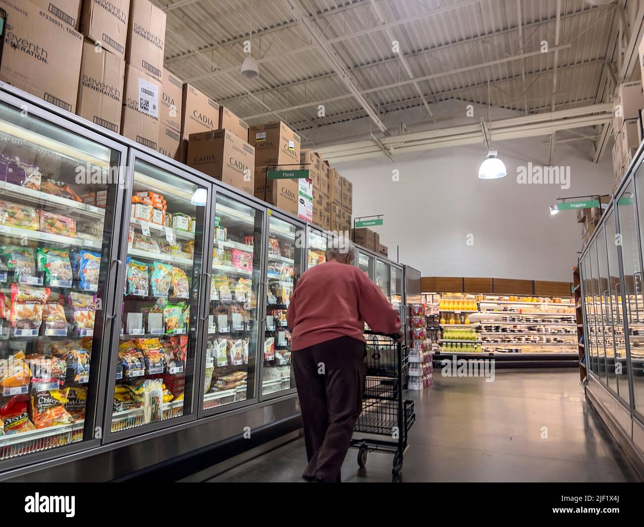 Mill Creek, WA USA - circa May 2022: Angled view of an older woman in a pink hoodie shopping in the frozen food section of a Town and Country Market. Stock Photo