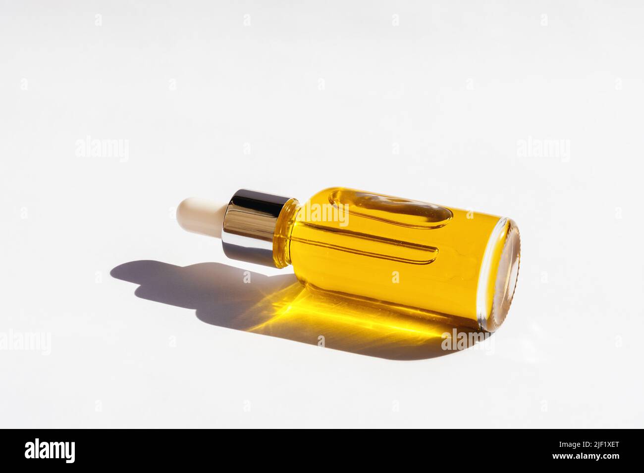 Dropper glass Bottle Mock-Up with metal lid and yellow essential oil lying on white background. Eco-cream, serum, cosmetics, massage oil. Natural light, beautiful orange sun shadows. Copy Space Stock Photo