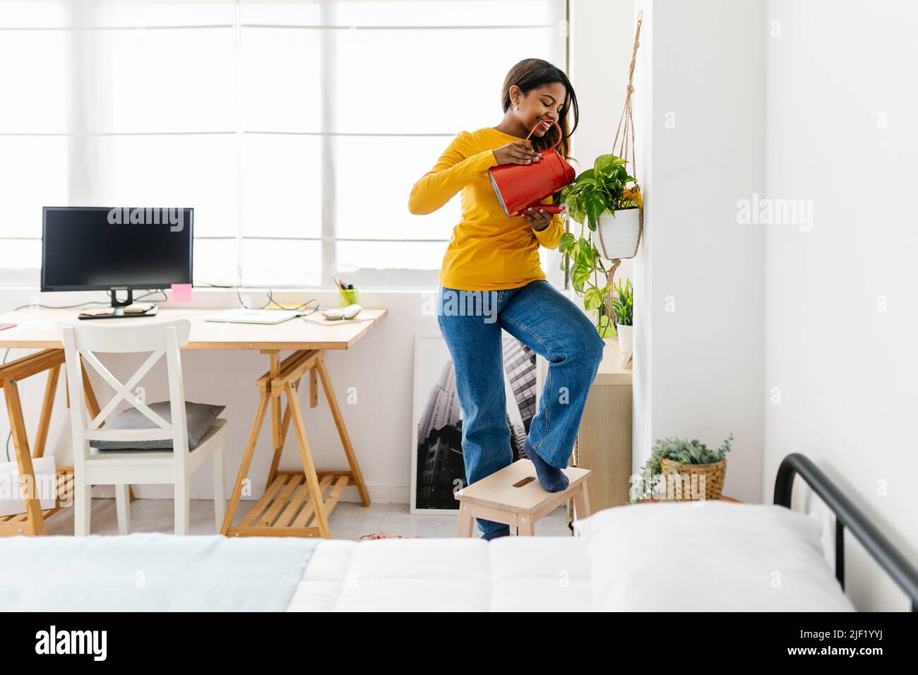 Young hispanic latina woman watering plants in her bedroom Stock Photo