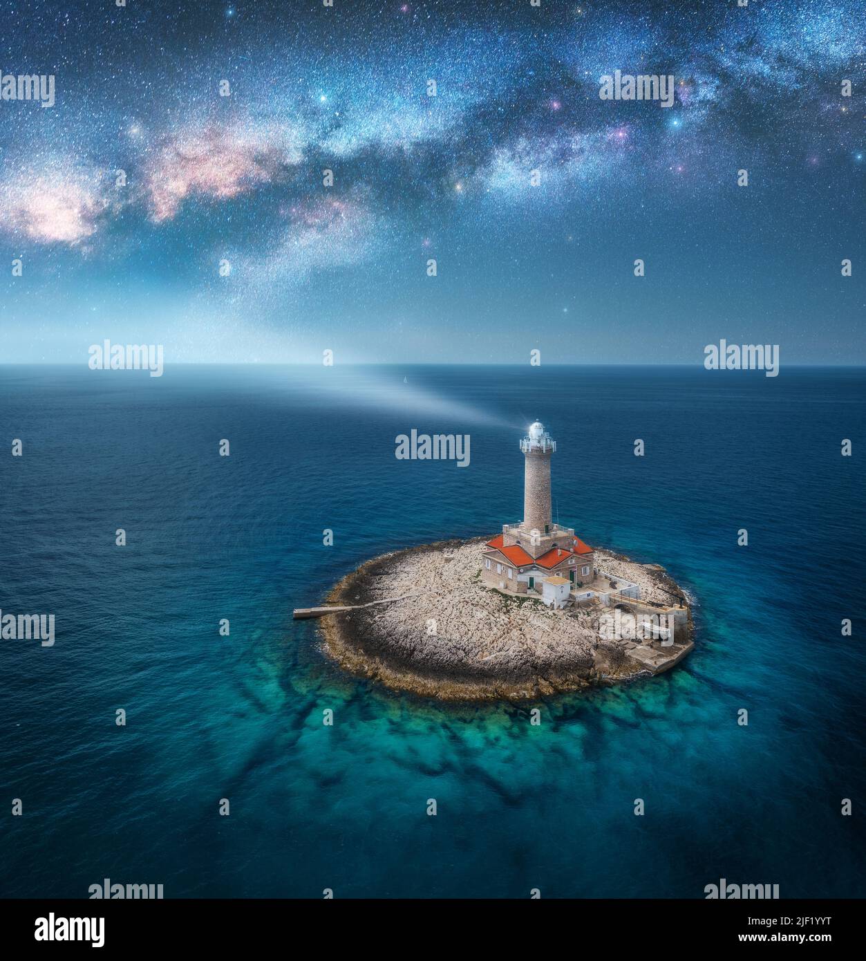 Lighthouse on smal island in the sea and Milky Way at night Stock Photo